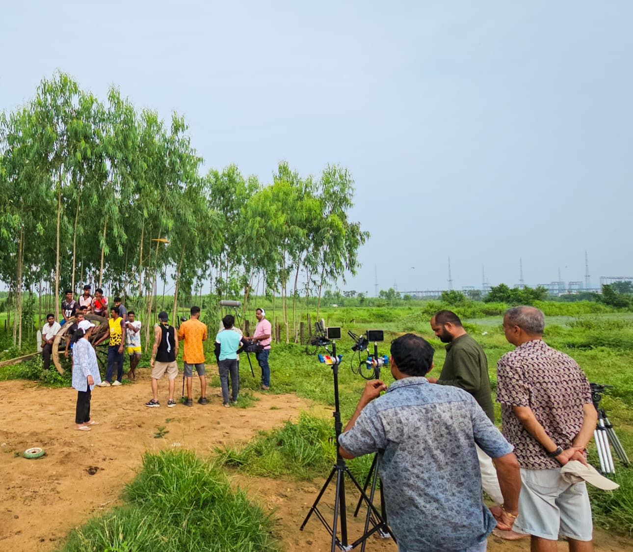 Crew setting up a camera on open ground beside the trees